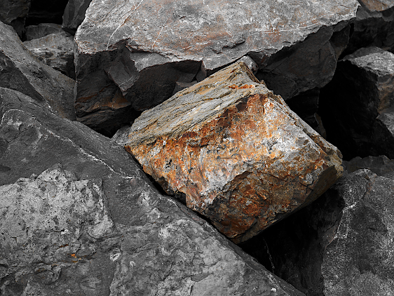 Paysage marin entièrement minéral: un bloc de forme presque cubique, de couleur orange, est enchâssé de tous côtés par d'autres rochers, gris et plus gros.